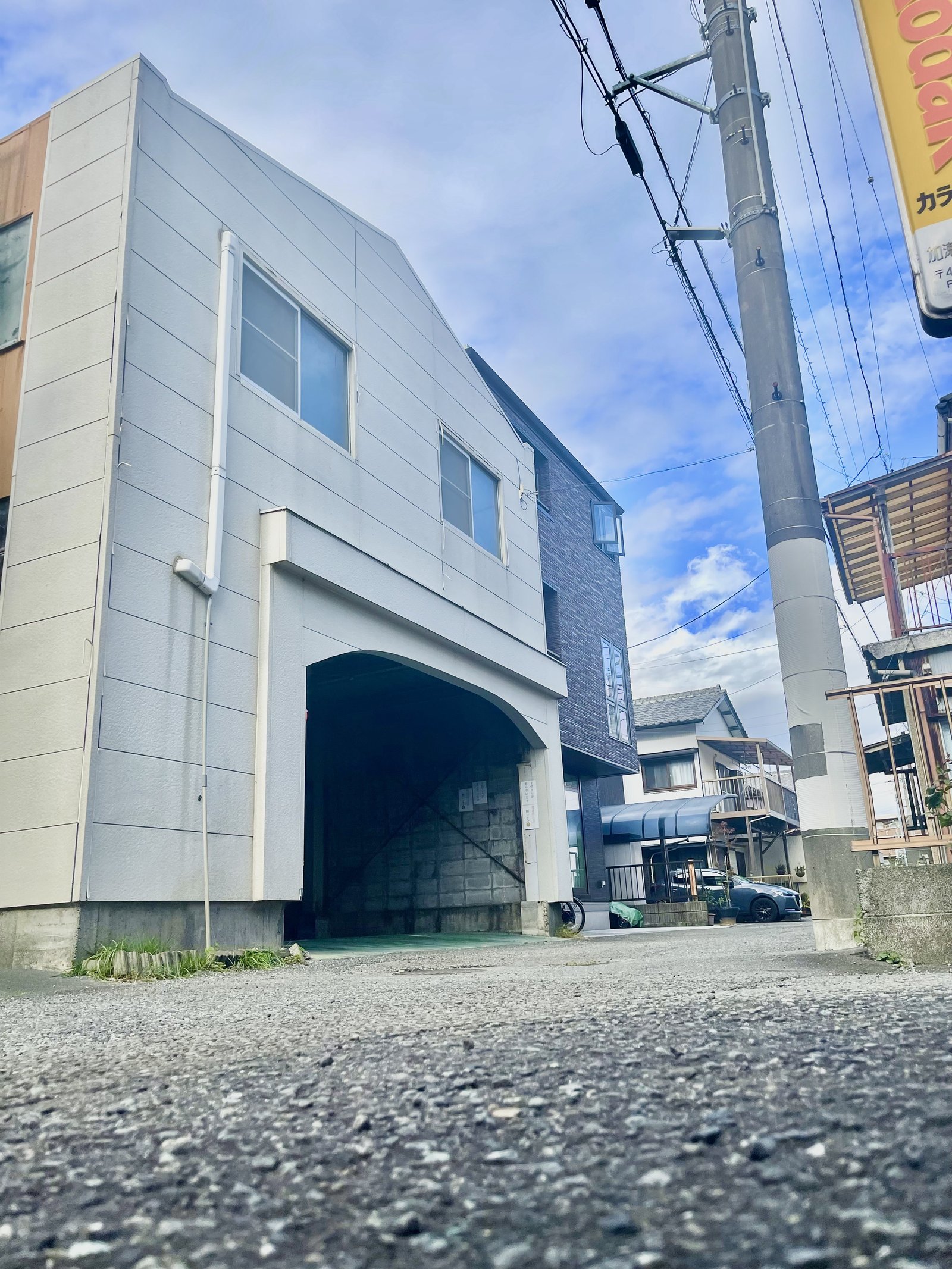 About The Fit の外観（グレー外壁の建物と、屋根付きの駐車場入口）